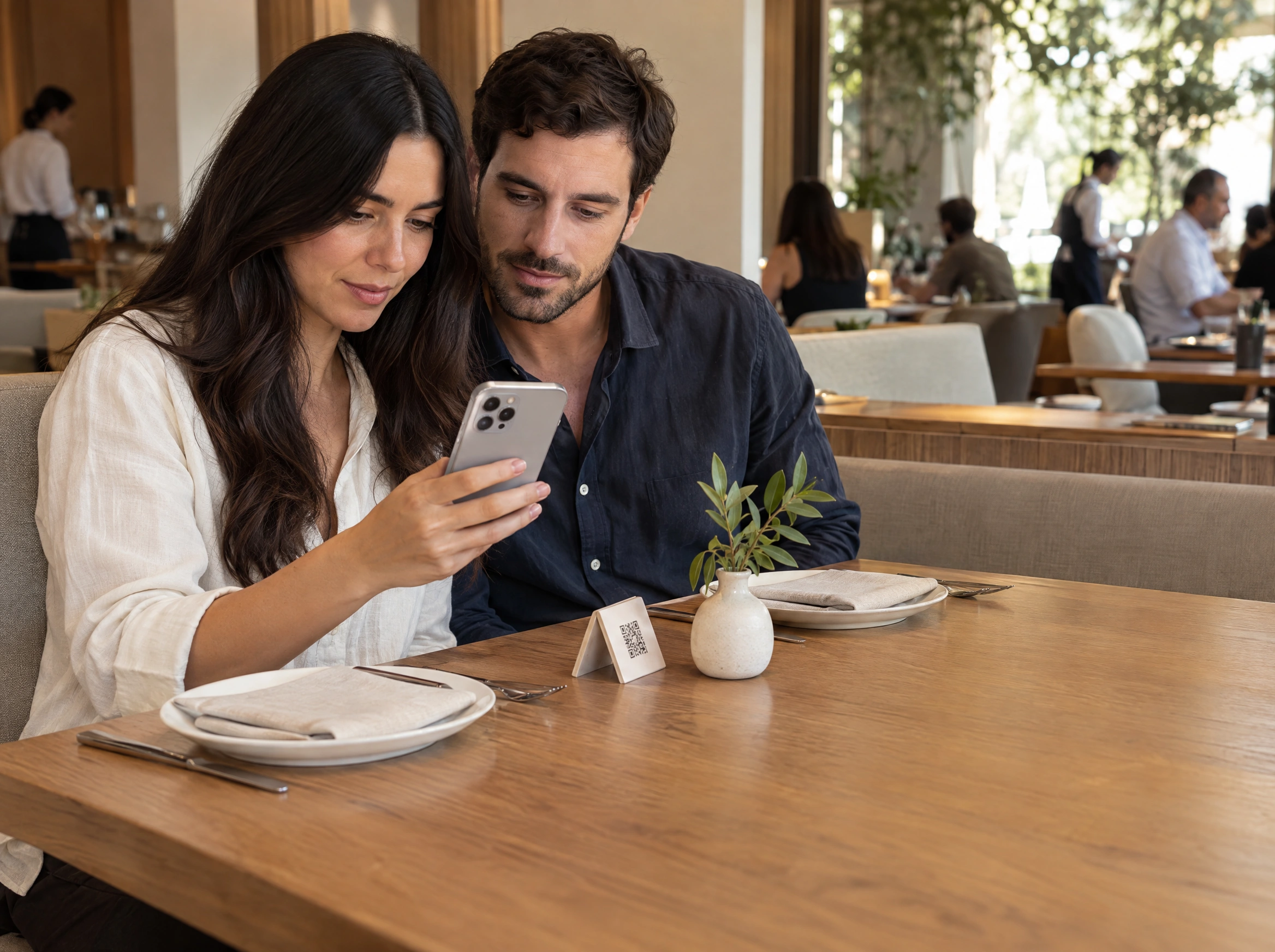 Two restaurant guests looking at the menu together on an iPhone beside their table QR